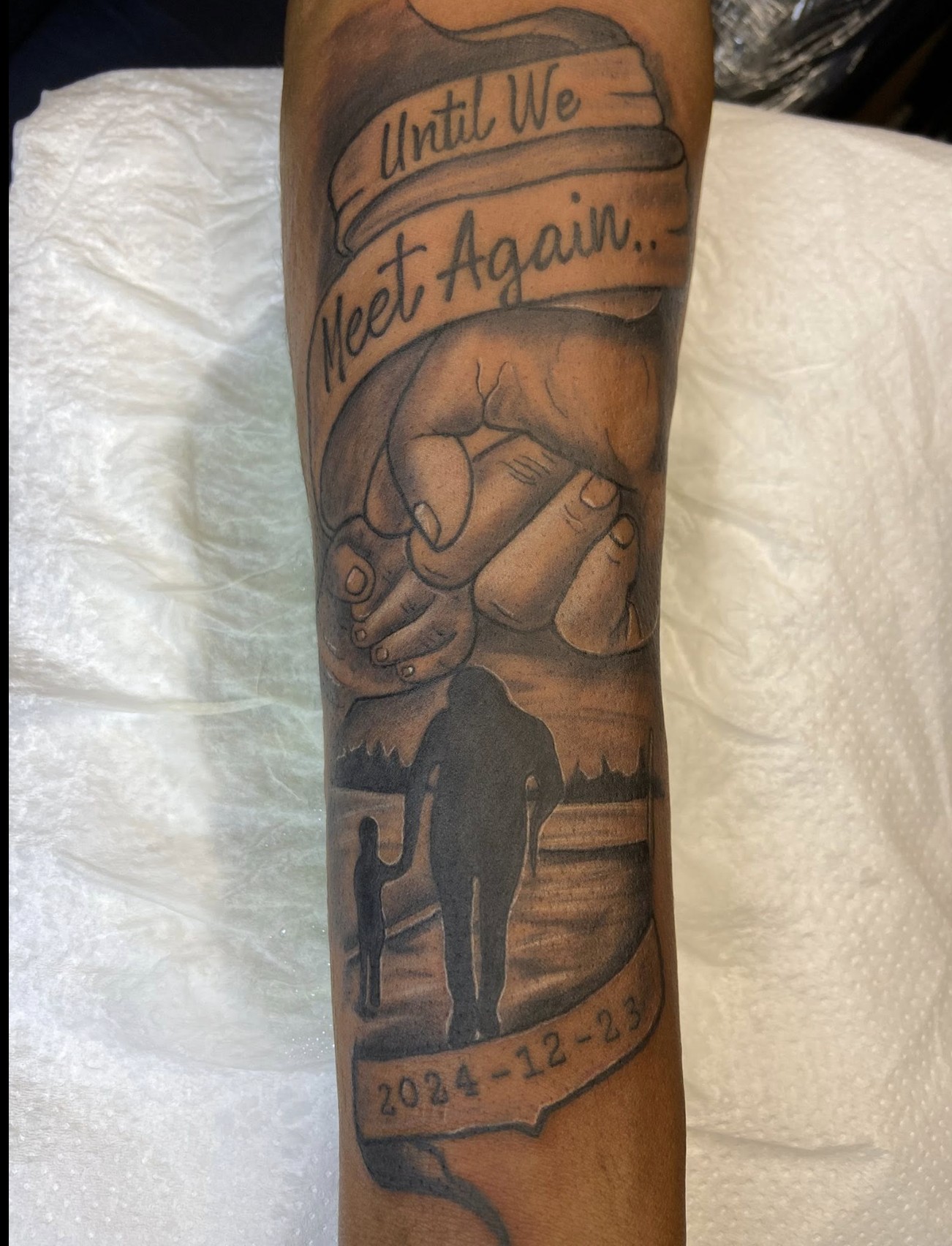 Memorial forearm tattoo with 'Until We Meet Again' banner, clasped hands and elephant silhouette dated 2024-12-23 — by Professional Black Ink