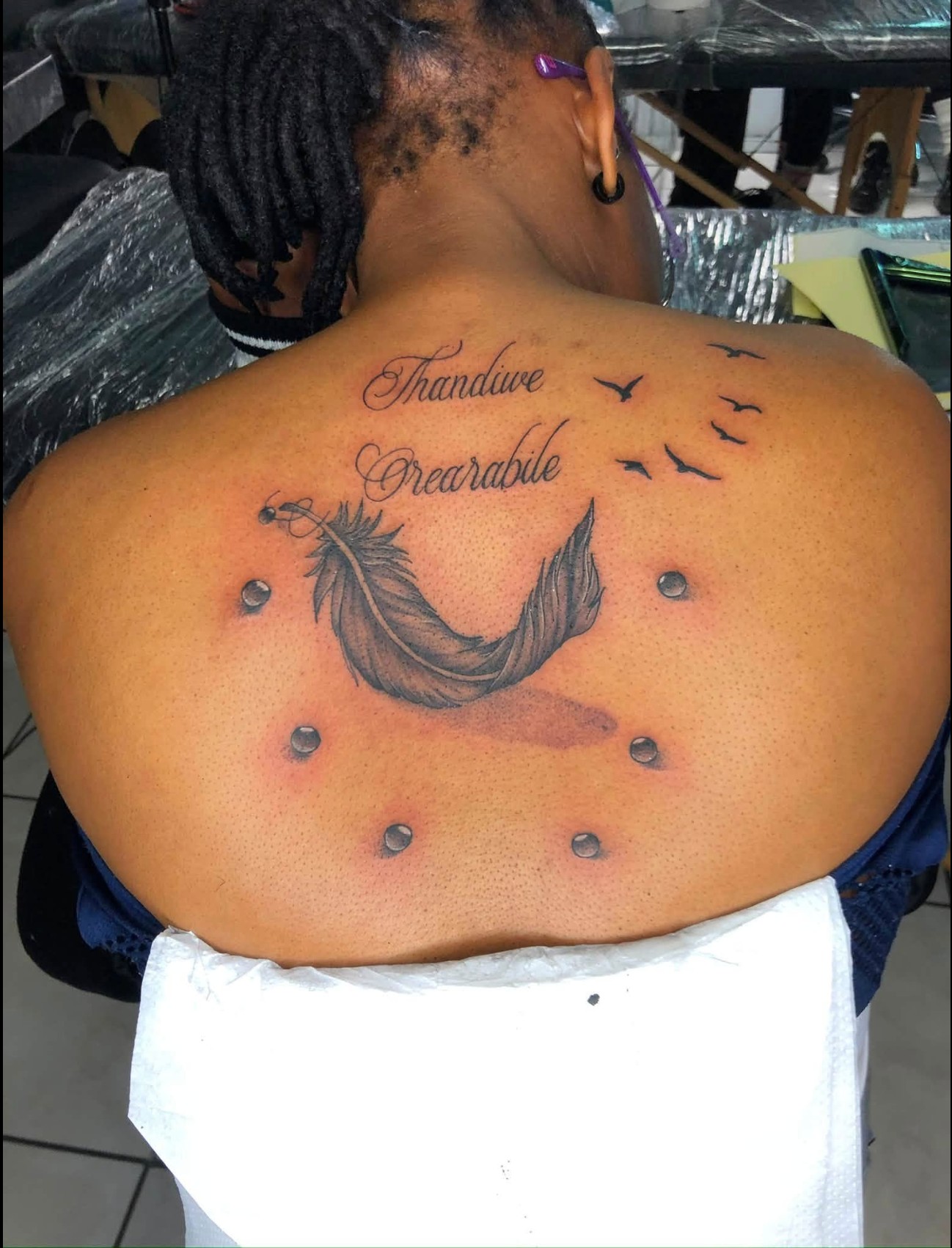 Feather and birds back tattoo with the names Thandiwe and Orearabile in script — by Professional Black Ink