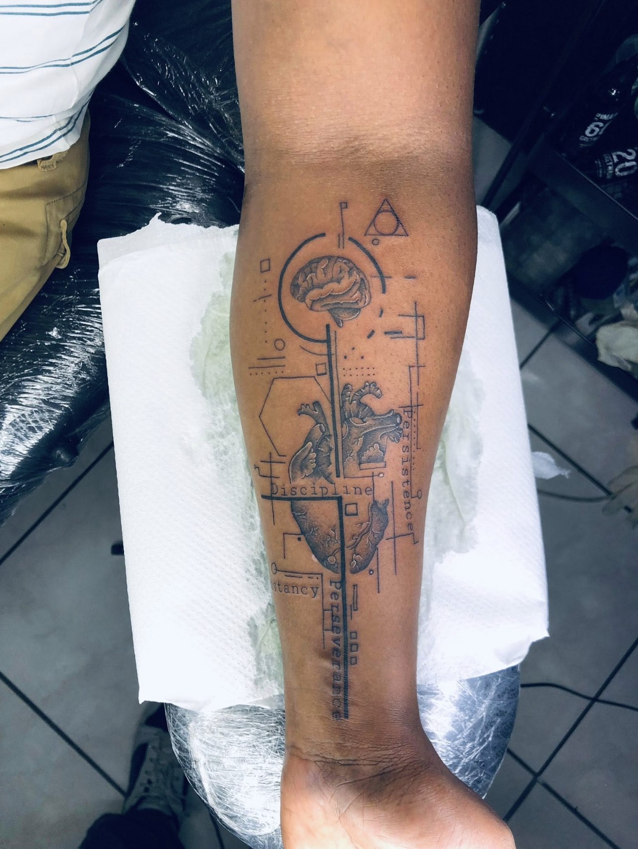 Fine-line geometric anatomical tattoo — brain and heart with the words Discipline, Persistence, Perseverance — by Professional Black Ink